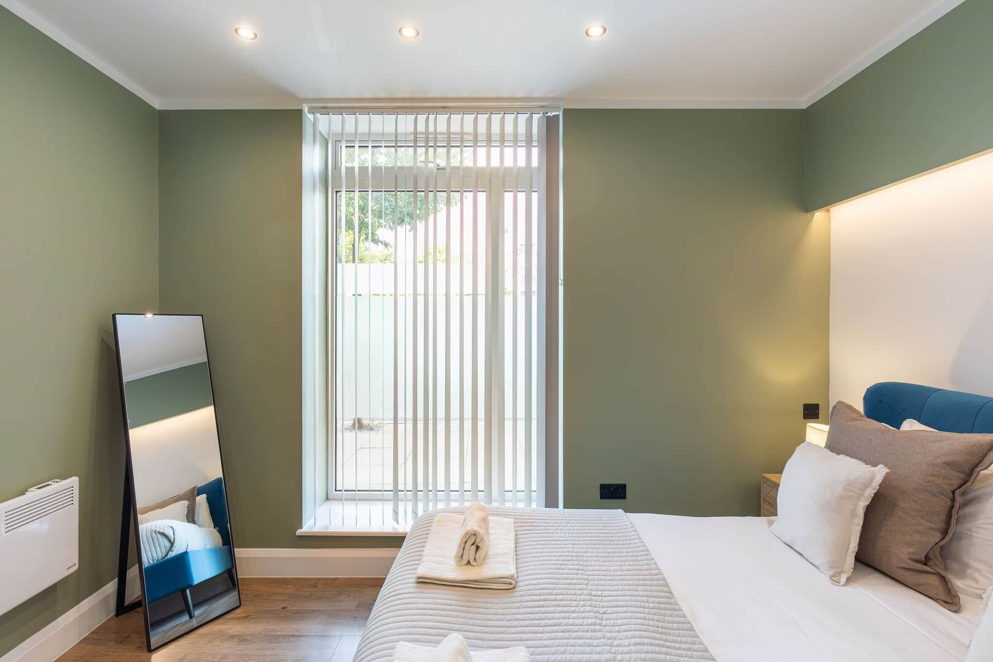 A bedroom with a bed, a large mirror, a nightstand, and a window with blinds.
