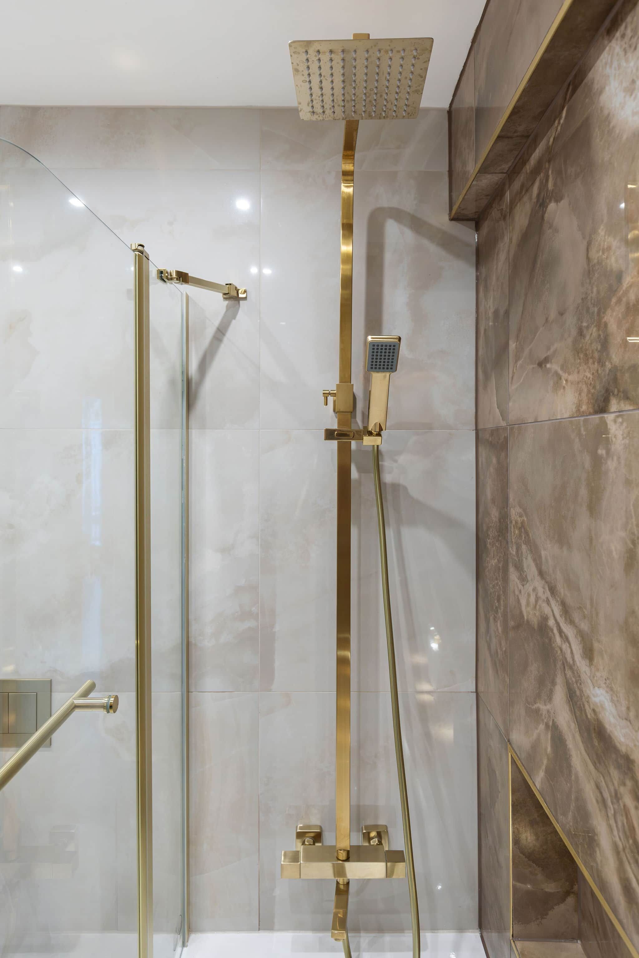 A modern bathroom with a glass-enclosed shower, a gold-colored showerhead, and a handheld showerhead.