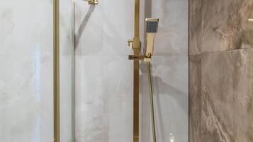 A modern bathroom with a glass-enclosed shower, a gold-colored showerhead, and a handheld showerhead.