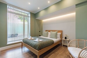 A bedroom with a bed, bedside table, lamp, and a view through a window. - Luxurious & spacious central modern 2bed flat (London)