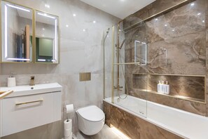 A modern bathroom with a glass-enclosed shower, a white toilet, a vanity with a mirror, and a marble backsplash. - Luxurious & spacious central modern 2bed flat (London)
