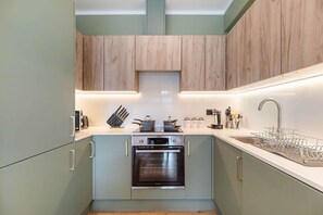 A compact kitchen with a built-in oven, a sink, and wooden cabinets. - Luxurious & spacious central modern 2bed flat (London)