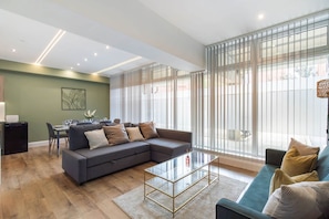 A modern living room with a sectional sofa, a glass coffee table, and a dining area with a table and chairs. - Luxurious & spacious central modern 2bed flat (London)