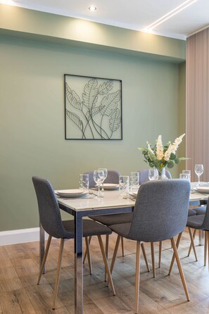 A dining area with a table set for four, chairs with wooden legs, and a wall-mounted artwork. - Luxurious & spacious central modern 2bed flat (London)