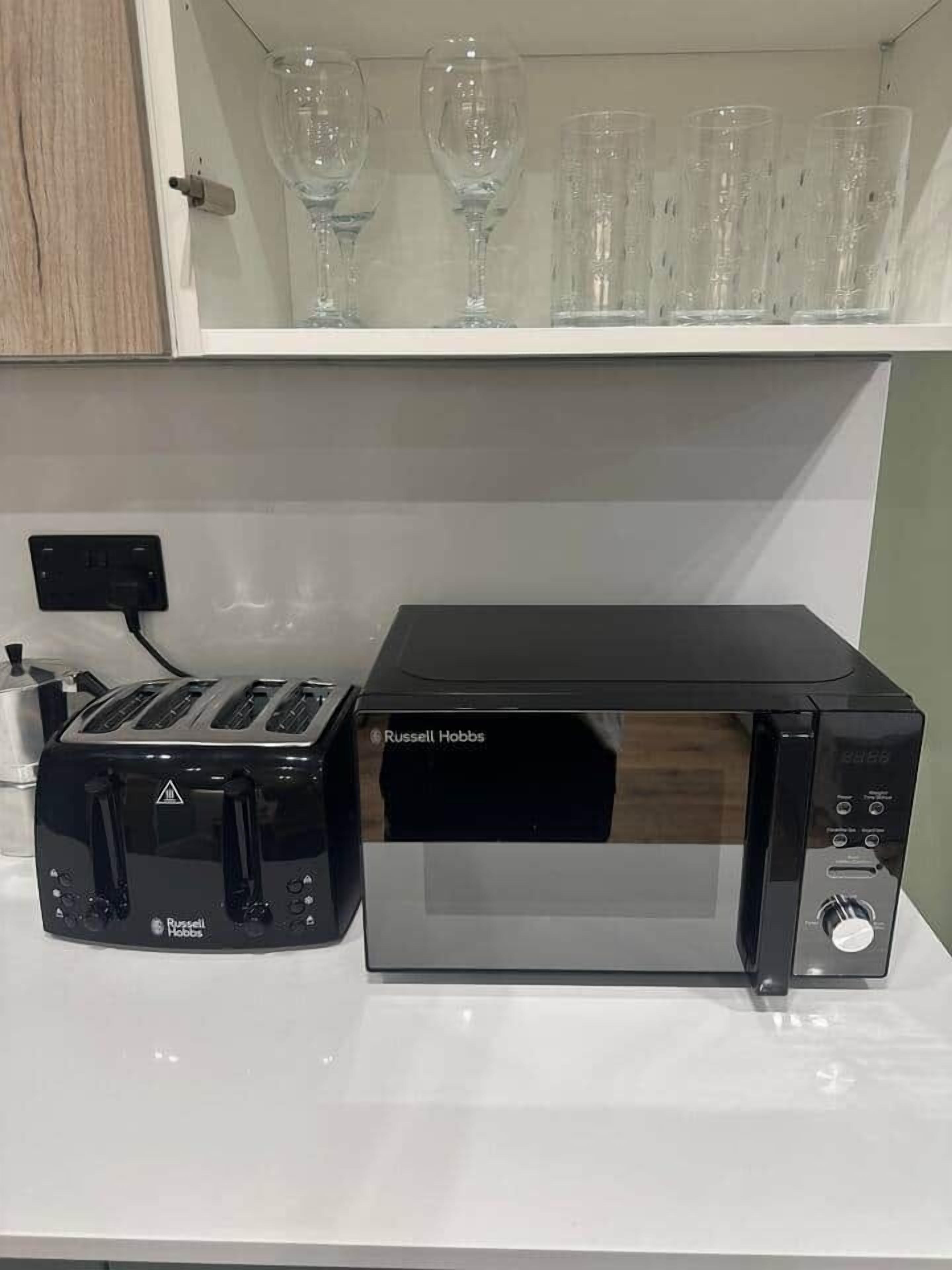 A kitchen with a toaster, a microwave, and a cabinet above holding wine glasses.