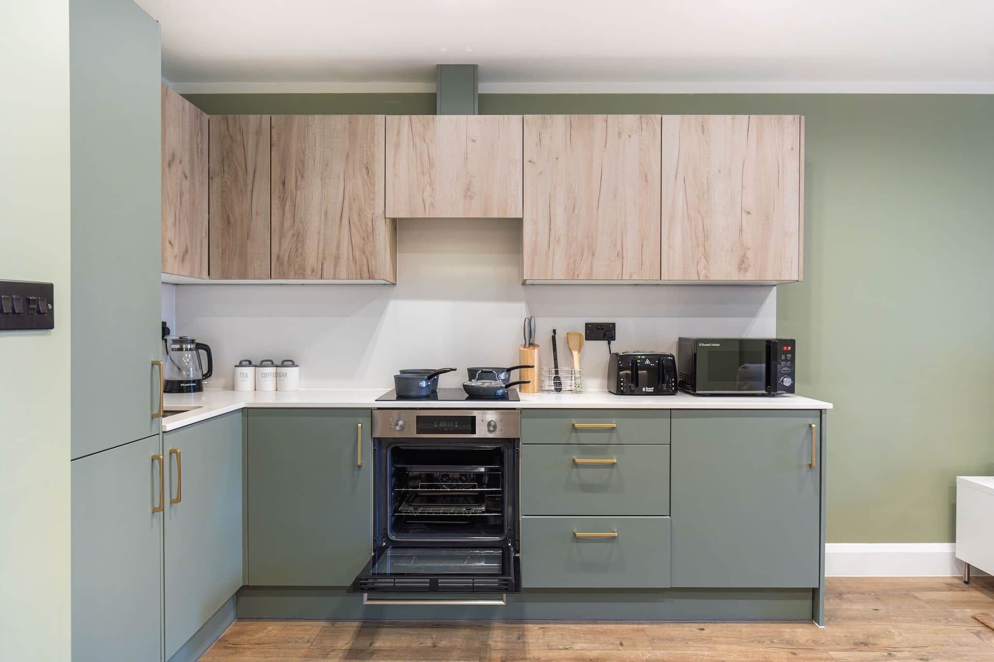 A compact kitchen with light wood cabinets, a built-in oven, and a microwave on the countertop.