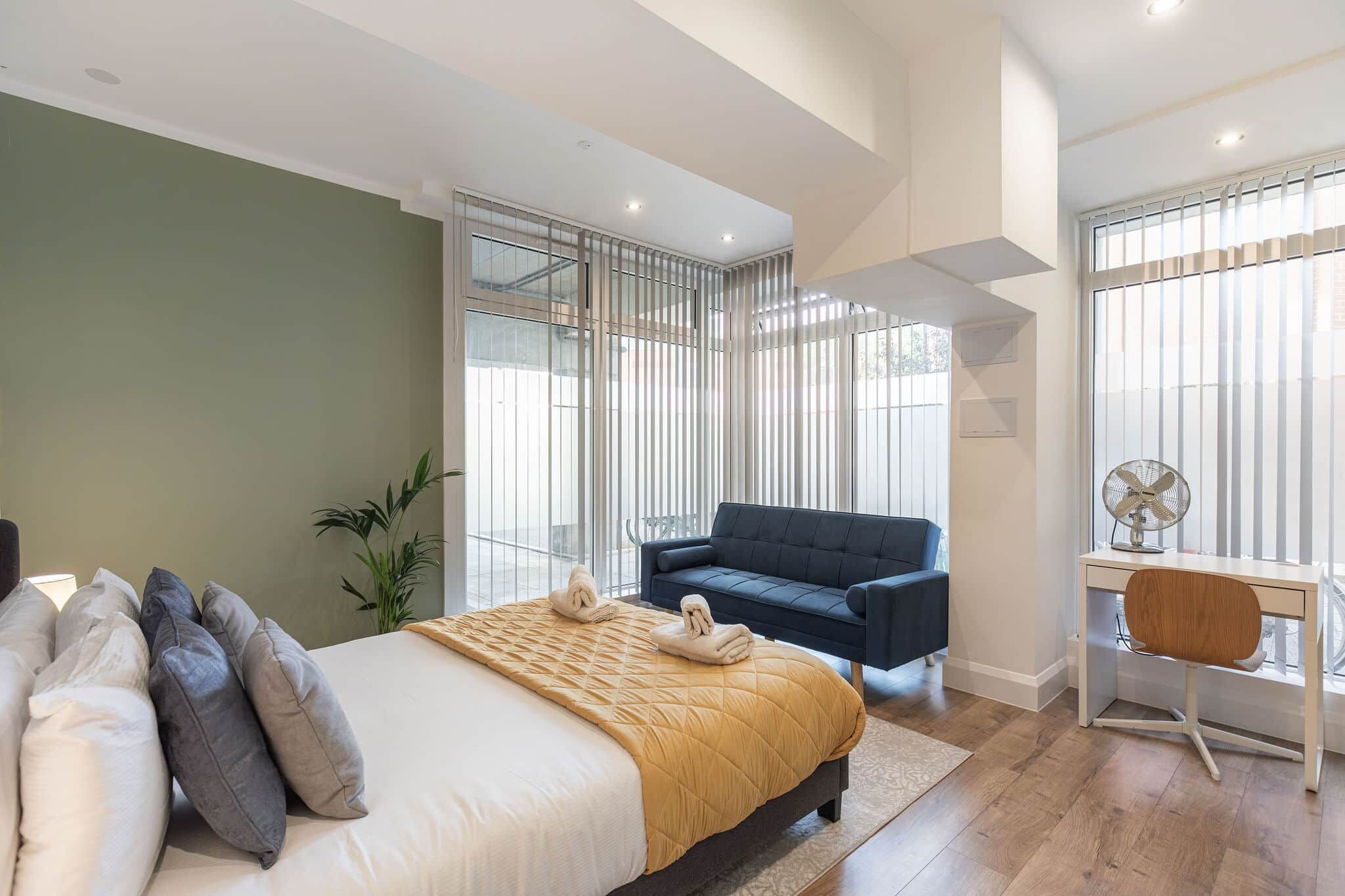 A modern bedroom with a bed, a desk, a chair, a sofa, and a large window.