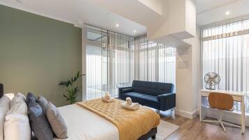 Une chambre moderne avec un lit, un bureau, une chaise, un canapé et une grande fenêtre.