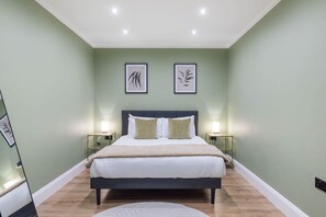A bedroom with a bed, two bedside tables, a nightstand, and framed artwork on the wall. - Stunning spacious modern central flat free parking (London)
