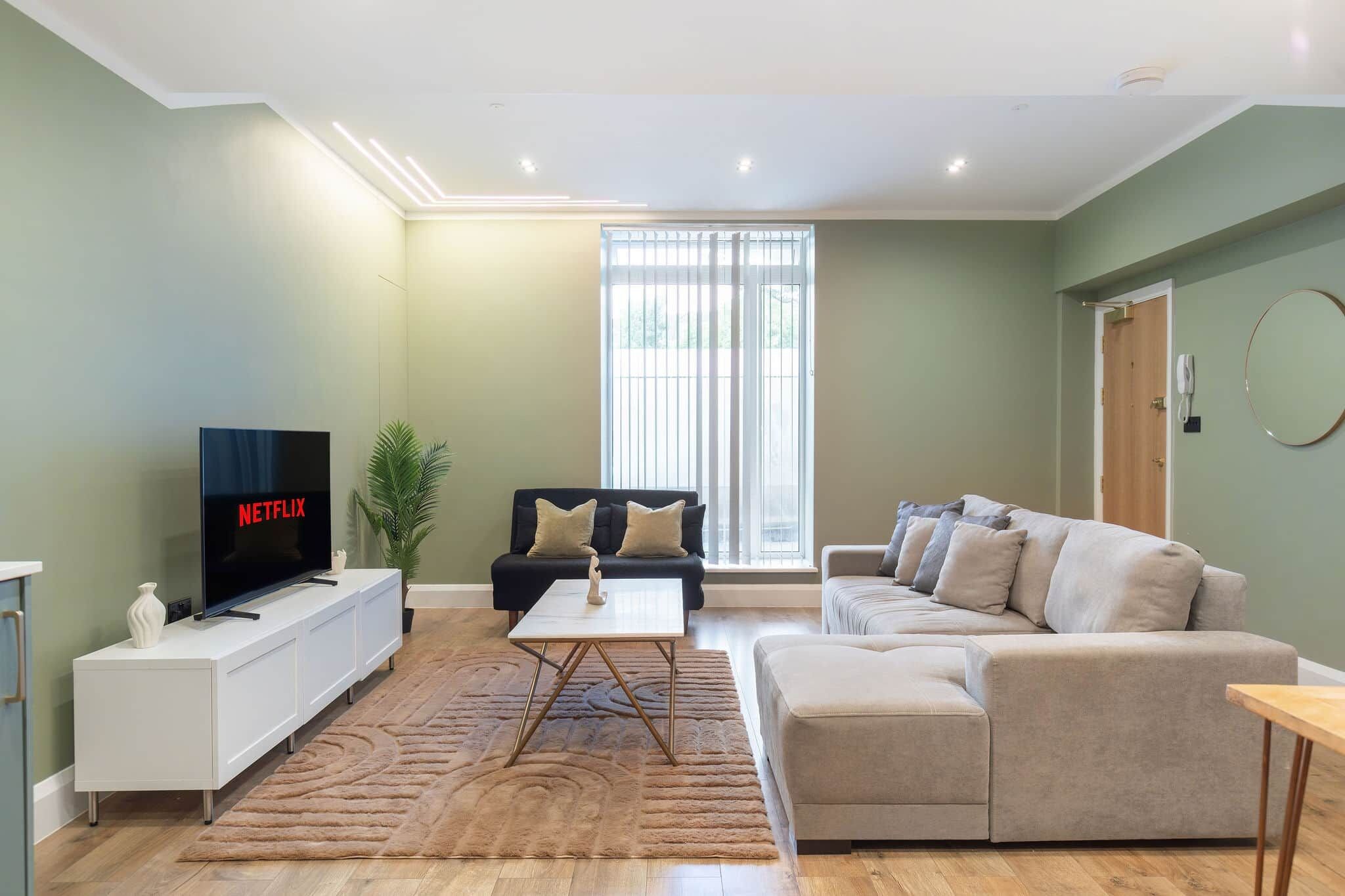 A living room with a flat-screen TV, a sofa, a coffee table, and a large window.
