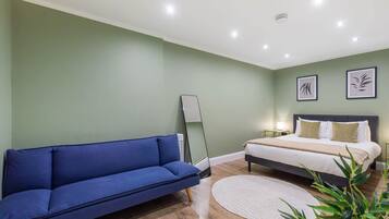 Ein Schlafzimmer mit einem Bett, einem blauen Sofa, einem Nachttisch, einer Lampe und gerahmten Kunstwerken an der Wand.