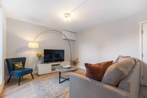 Un salon moderne avec un téléviseur à écran plat, un canapé, un fauteuil et une table basse.