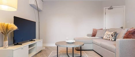 Een moderne woonkamer met een flatscreen televisie, een ronde salontafel, een grijze bank en een decoratieve vaas.