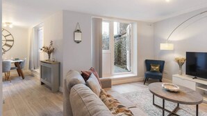 Un salon moderne comprenant un canapé, un coin repas avec une table et des chaises, un téléviseur et une grande fenêtre donnant sur un mur de briques.
