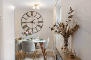 A dining area with a large wall clock, a table set for two, and a vase with dried flowers. - Stylish 2BR Georgian Flat • Prime Camden Location (London)