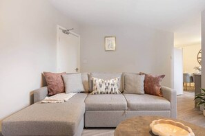 A modern living room with a grey sofa, a side table, and a framed picture on the wall. - Stylish 2BR Georgian Flat • Prime Camden Location (London)