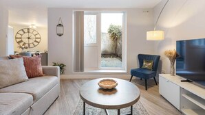 Un salon moderne avec un canapé, un fauteuil, une table basse, un téléviseur et une grande fenêtre.