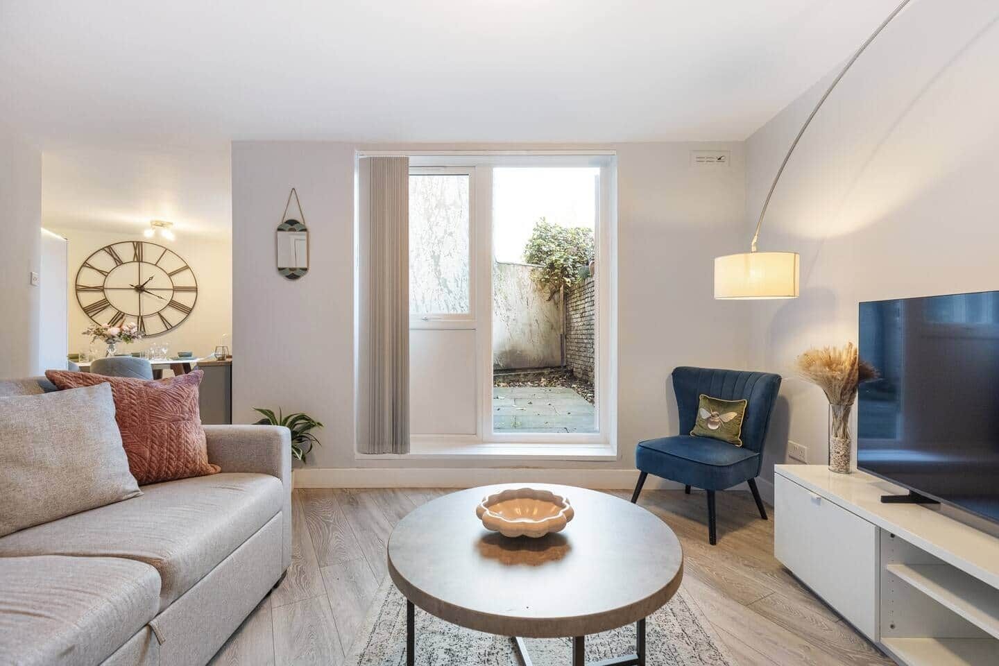 Un salon moderne avec un canapé, un fauteuil, une table basse, un téléviseur et une grande fenêtre.
