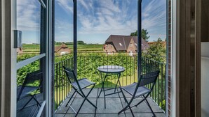 Ein Balkon mit Tisch und Stühlen, Blick auf eine grüne Landschaft und einen klaren Himmel.