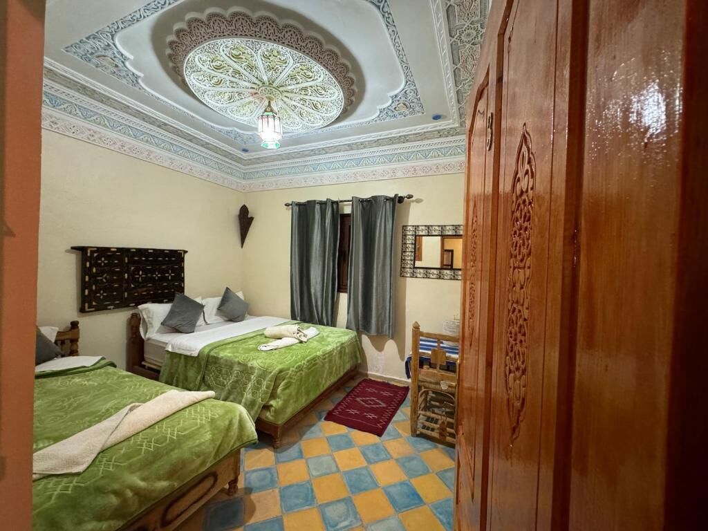 A room with two beds, a patterned ceiling, and a wooden door.
