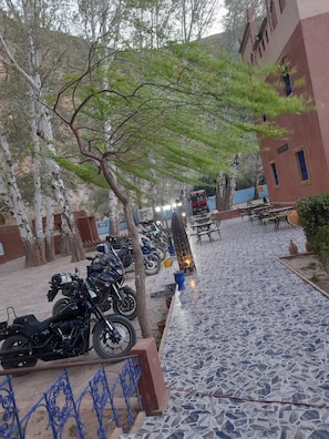 Une cour pavée où sont garées des motos, avec des tables et des chaises à l’extérieur, et un bâtiment à la façade rouge.
