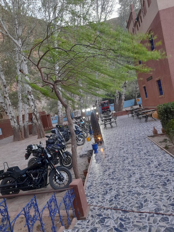 Un patio empedrado con motocicletas estacionadas, mobiliario de exterior y un edificio de fachada roja.