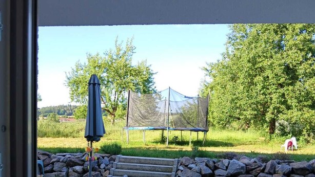 Una veranda esterna con pavimento in pietra, un tavolo e sedie, e una zona coperta con una tenda.