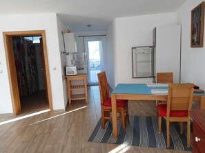 Uma área de refeições com uma mesa e cadeiras, uma cozinha ao fundo e uma porta que dá para outro cômodo.