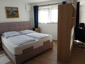 A bedroom with a bed, a nightstand, a chair, a wardrobe, a painting, and a window with curtains.