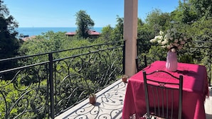 Un balcón con mesa y silla, un jarrón de flores y vista al mar.