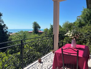 Un balcon avec une table et une chaise, un vase de fleurs et une vue sur la mer.