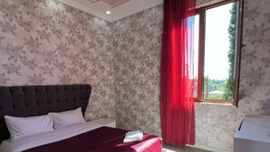 Un dormitorio con cama, una ventana con cortinas rojas y vistas al exterior.