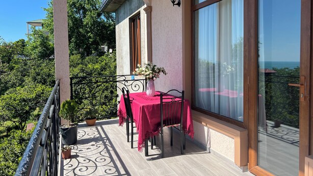 Un balcón con una mesa para dos, una planta en maceta y vistas a la vegetación y un paisaje lejano.