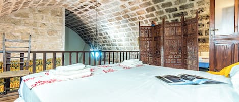A bedroom with a stone ceiling, a bed with white linens, a wooden wardrobe, and a wooden chair.