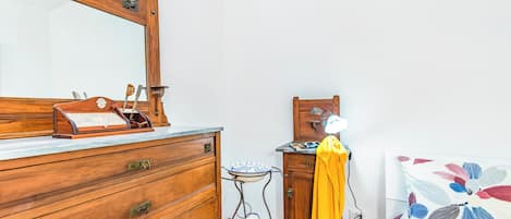 A wooden dresser with drawers, a mirror, a small table with a blue and white vase, and a bed with a floral bedspread.