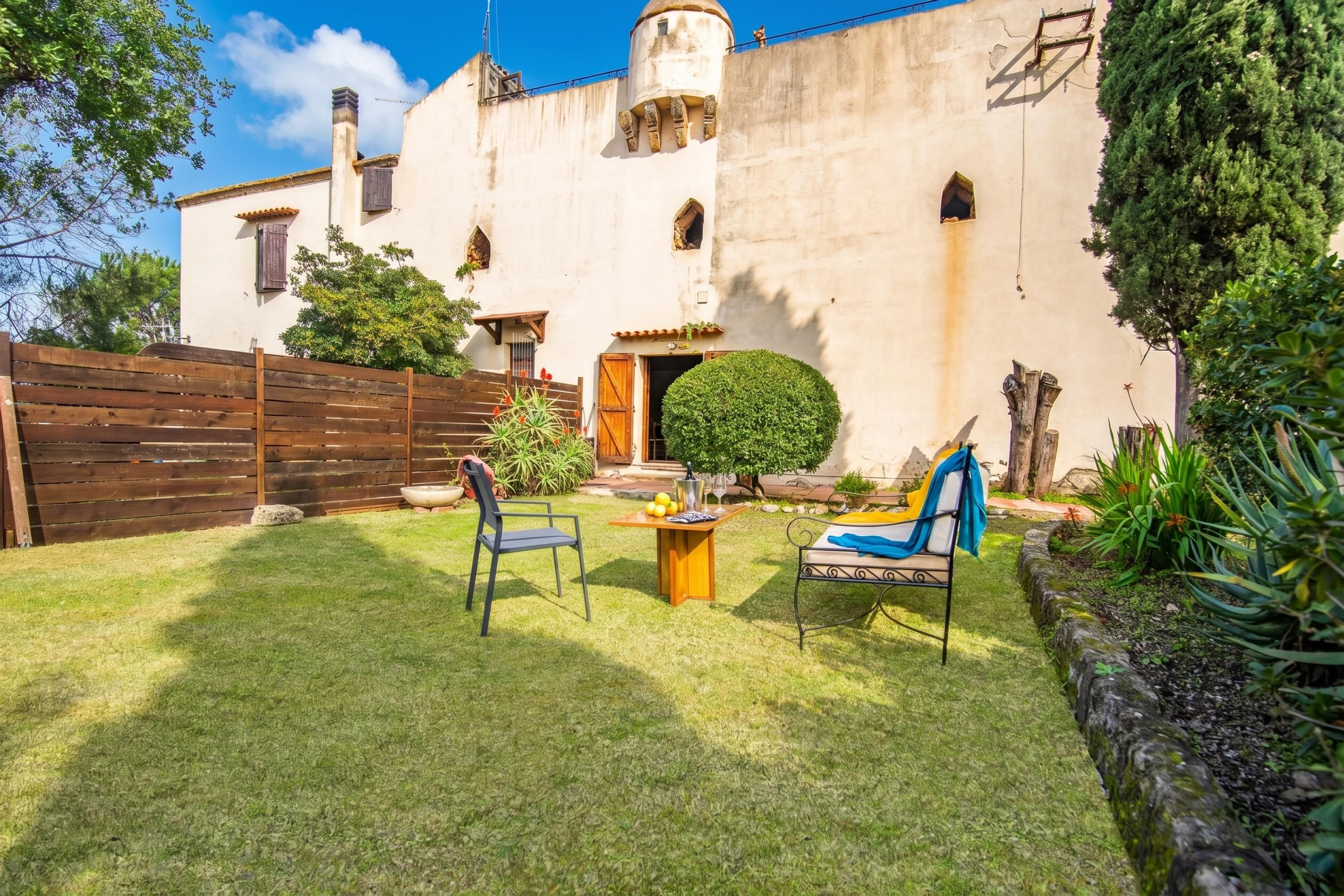 A courtyard with a wooden fence, a small table with chairs, and a building with a tiled roof and a round window.