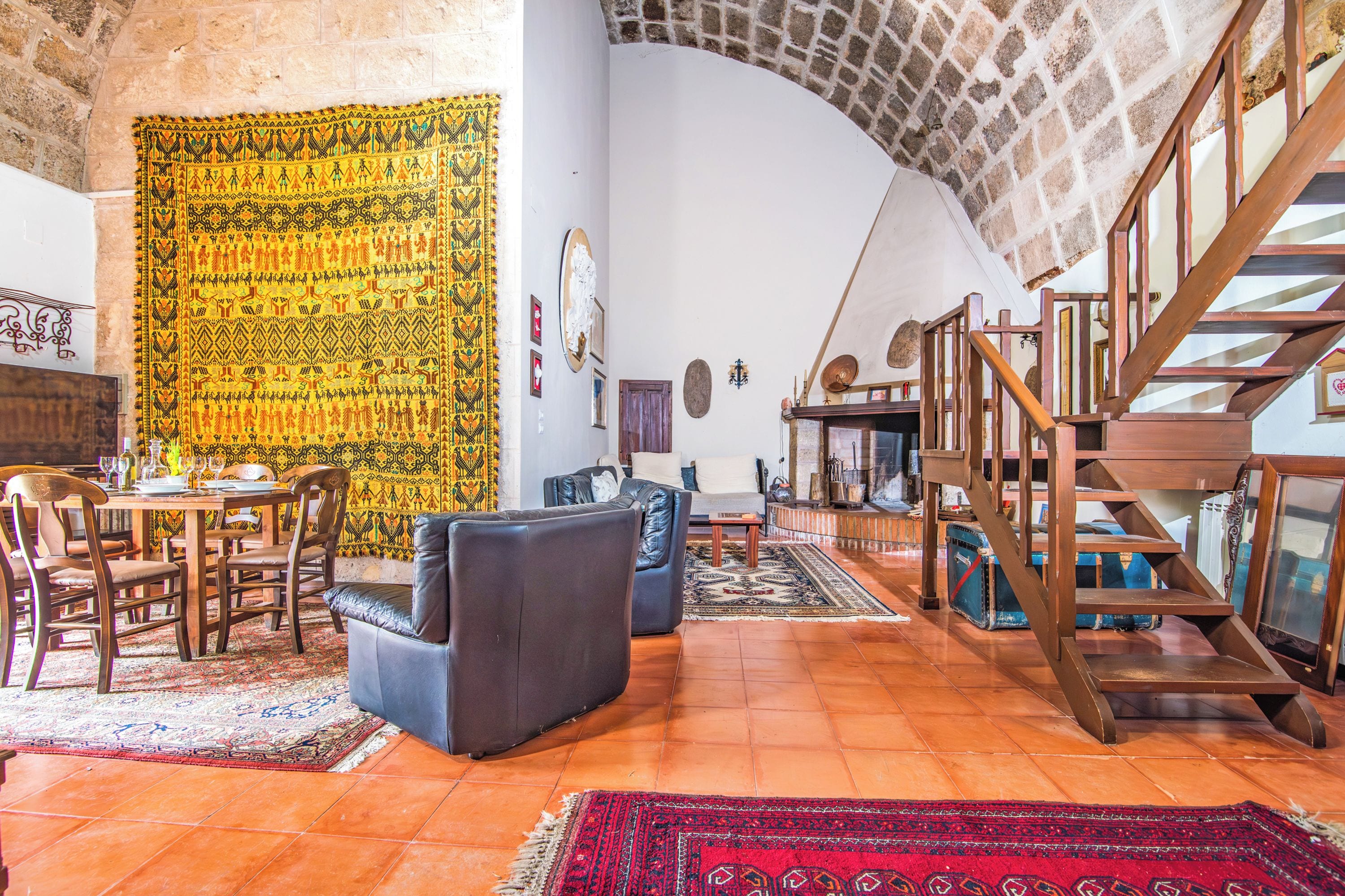 A spacious living area with a dining table, sofas, a staircase, and a patterned tapestry.