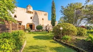 A building with a dome and arched windows, surrounded by a well-maintained garden with a lawn and various shrubs. - Fort Galante (Alghero)