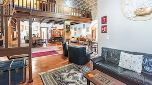 A spacious living area with a high ceiling, a wooden staircase, and a dining area with a piano. - Fort Galante (Alghero)