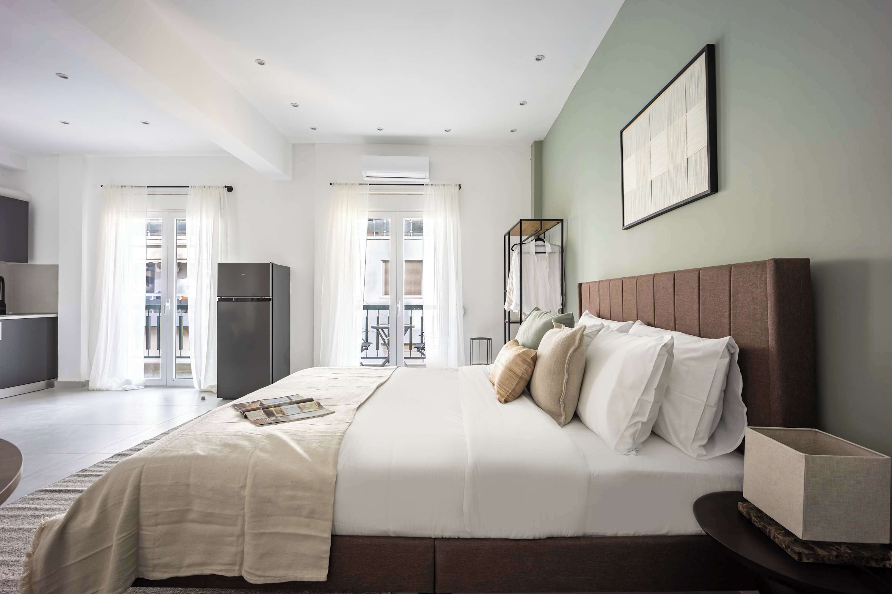 A modern bedroom with a large bed, a bedside table, a wardrobe, and a view of the outside.
