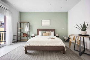 A bedroom with a bed, bedside tables, a chair, a small table, a potted plant, a window with curtains, and a view of buildings outside. - Stylish Studio l Balcony l No Elevator (Athens)
