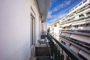 Un balcón con mesa y sillas, una ventana y vistas a edificios cercanos.