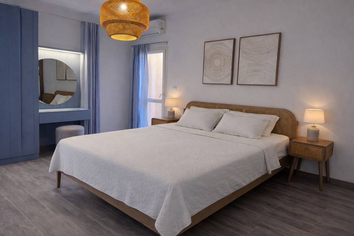 A bedroom with a bed, bedside lamps, a mirror, and two wall art pieces.