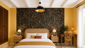 Une chambre à coucher avec un grand lit, un bureau, une chaise, une lampe et un mur orné d’un motif floral.