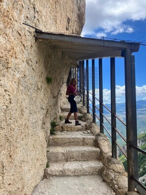 A person walking on a stone staircase with a metal railing, overlooking a mountainous landscape.