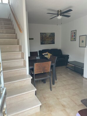 A staircase leading to a living area with a dining table, chairs, a sofa, and a ceiling fan.