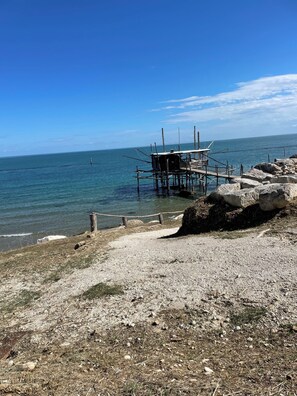 A coastal scene with a wooden pier extending into the sea, surrounded by rocks and pebbles.