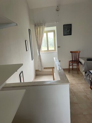 A room with a staircase, a window with curtains, a wooden chair, and a bed.