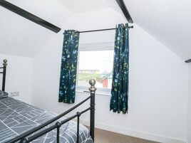Un dormitorio con cama, ventana con cortinas, vista de edificios y techo con vigas a la vista.