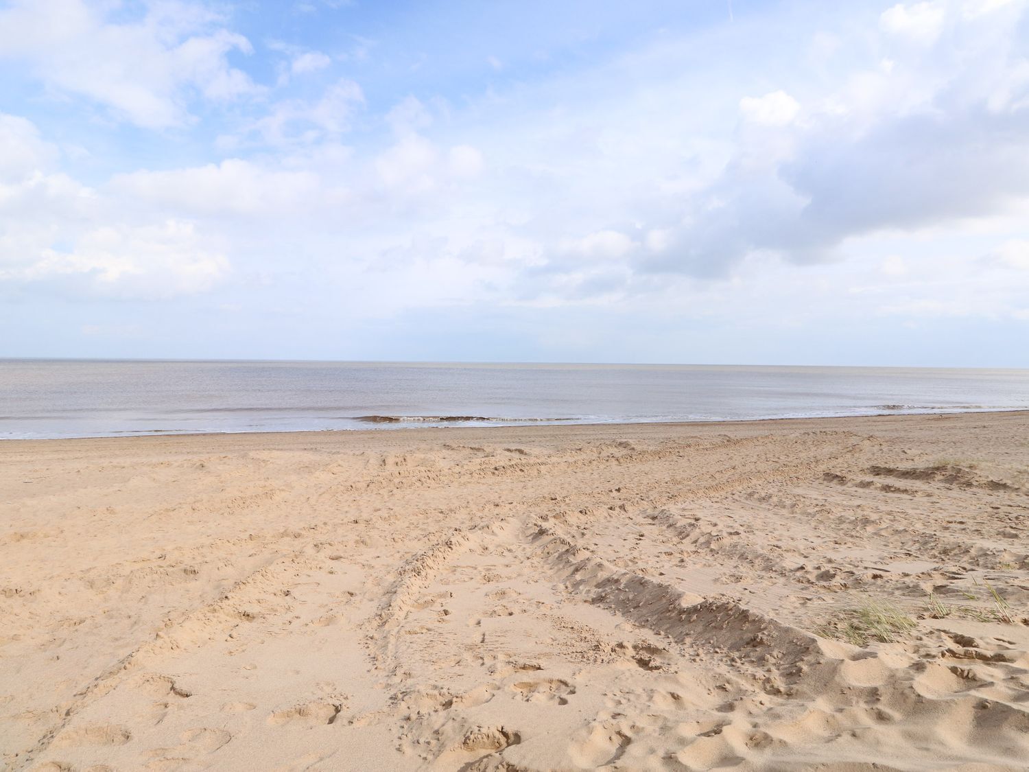 A sandy beach with footprints and a calm sea under a partly cloudy sky.